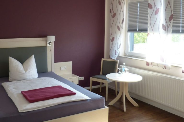 Einzelzimmer Hotelzimmer mit Einzelbett, Tisch und Stuhl, bordeauxroter Wand und hellem Fenster.